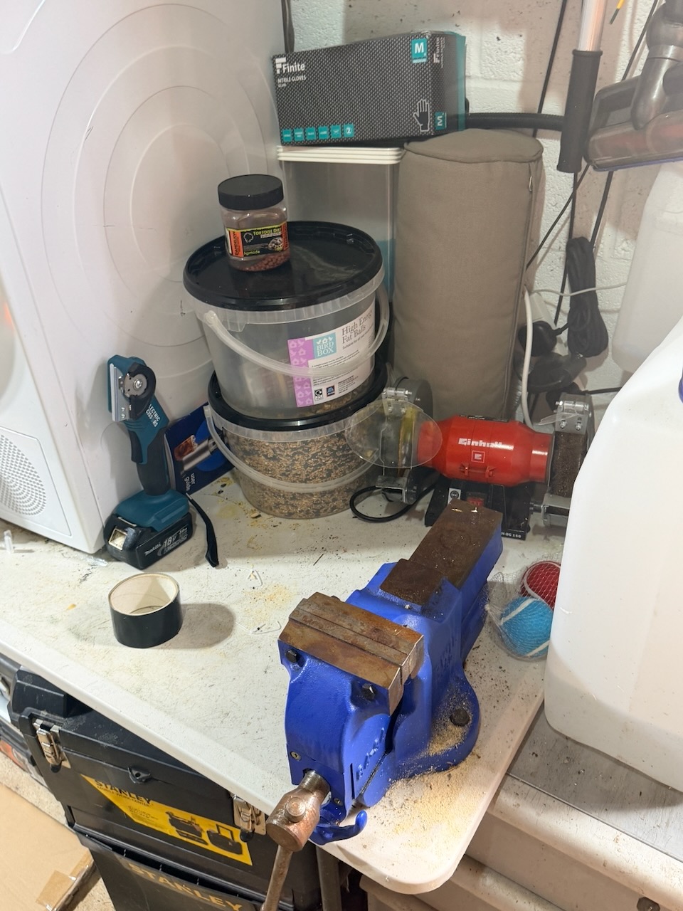 Blue bench vice fixed to a pasting table beside bird seed and household appliances